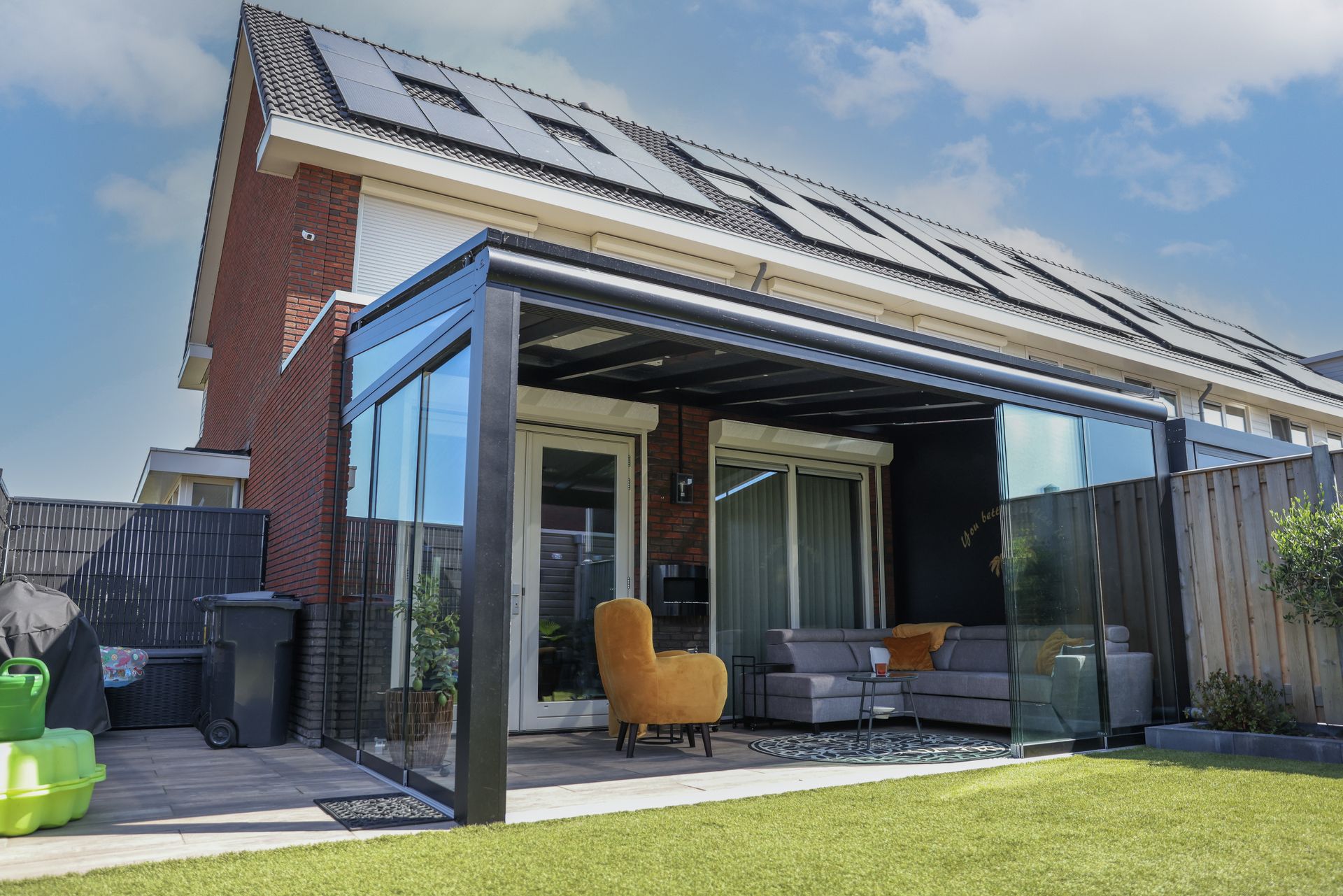 Haus mit verglaster Terrasse, auf der ein graufarbiges Sofa und ein gelber Sessel stehen